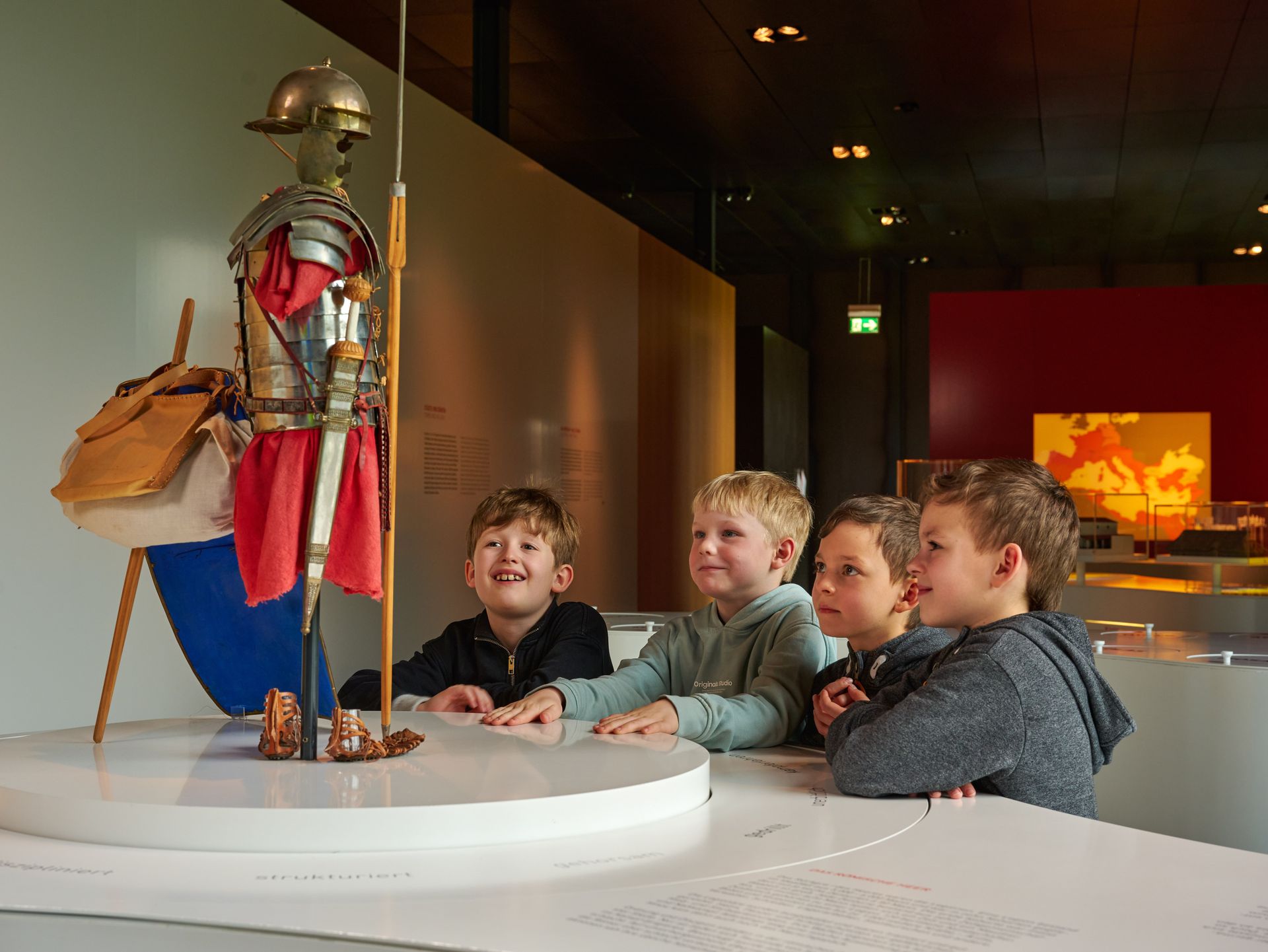 Vier Kinder bestaunen die verkleinerte Nachbildung von Legionärsausrüstung.